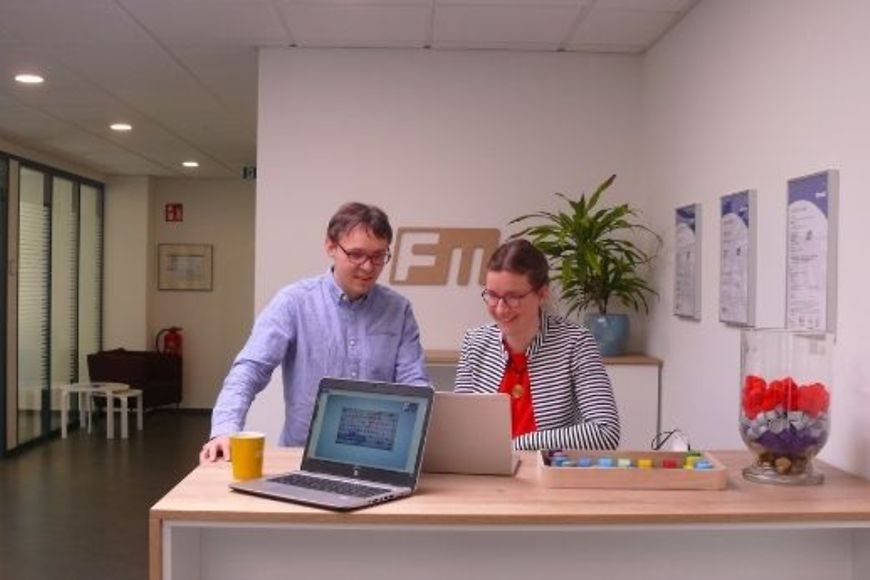 Ein Mann und eine Frau in einem Büro an einem Stehtisch, beide schauen in einen Laptop.